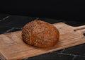 Rundes, rustikales Brot mit goldbrauner, mit Körnern bestreuter Kruste liegt auf einem hellen Holzbrett