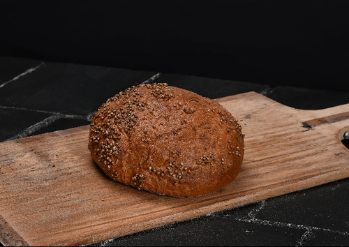 Rundes, rustikales Brot mit goldbrauner, mit Körnern bestreuter Kruste liegt auf einem hellen Holzbrett