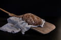 Rustikales längliches Bauernbrot mit kräftig gebräunter, bemehlter Kruste liegt auf einem Holzbrett und ist teilweise auf einem hellen Leinentuch arrangiert
