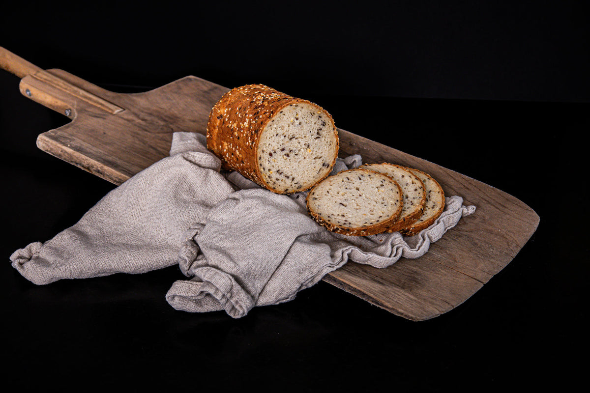 Rustikales Proteinbrot mit goldbrauner, mit Saaten bestreuter Kruste, aufgeschnitten und auf einem Holzbrett mit Leinentuch angerichtet