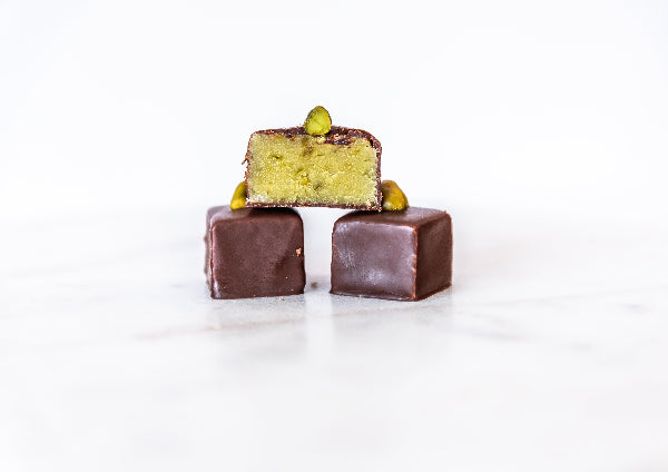 drei Schnittpralinen mit Zartbitterkuvertüre und Pistazien.
eine Praline ist angeschnitten und zeigt Pistazienmarzipan