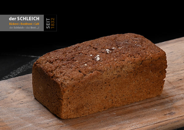Ein rechteckiges, kräftig gebräuntes Brot mit kompakter, leicht rissiger Kruste liegt auf einem Holzbrett. Die Oberfläche ist mit etwas Mehl bestäubt.